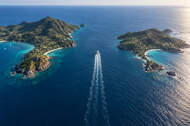Two Caribbean islands separated by open water with a single ferry wake crossing the channel between them